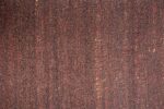 Modena Bruin Antraciet 522 200x300 heeft een gestructureerd oppervlak met een dichte vlek van kleine, donkerbruine zaden, geaccentueerd door af en toe rode en bruine zaden voor een natuurlijke, organische uitstraling.