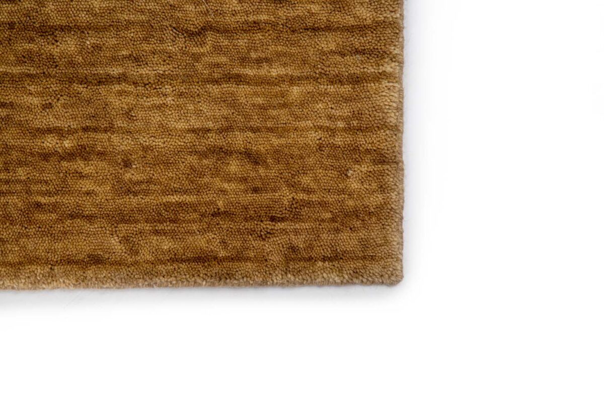Een close-up van de hoek van het San Stefano Dark Beige 08 200x300 vloerkleed, met het gestructureerde oppervlak en subtiele, onregelmatige patroon tegen een witte achtergrond.