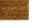 Een close-up van de hoek van het San Stefano Dark Beige 08 200x300 vloerkleed, met het gestructureerde oppervlak en subtiele, onregelmatige patroon tegen een witte achtergrond.
