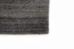 Close-up van de hoek van het Portofino Grey 03 200x300 vloerkleed, met een grijs gestructureerd oppervlak met subtiele horizontale lijnen, tegen een witte achtergrond.