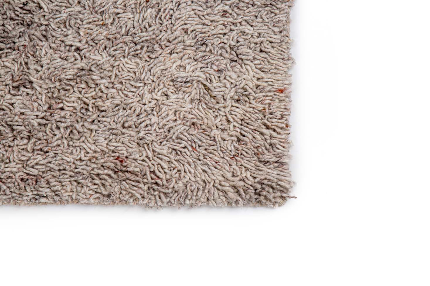 Een close-up van de hoek van het Berbero Lungo Beige 101 200x300 shaggy vloerkleed, met een lichtbruin gestructureerd oppervlak tegen een witte achtergrond.