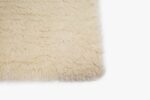 Close-up van de hoek van een Merano White 011 200x300 shagtapijt op een witte achtergrond. De crèmekleurige textuur ziet er zacht en dik uit.