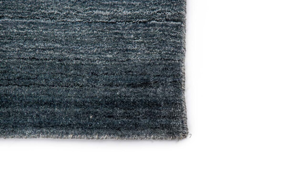Close-up van de hoek van het Portofino Blue 01 200x300 vloerkleed, met een donkerblauw en grijs geweven dessin op een witte achtergrond.
