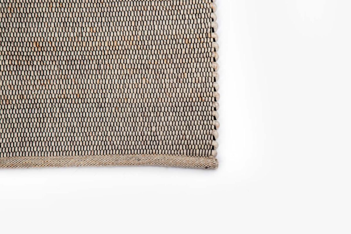 Een close-up van de hoek van het Bressano Light Beige 141 200x300 vloerkleed toont het eenvoudige, strak gebreide patroon tegen een schone witte achtergrond.