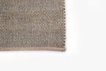 Een close-up van de hoek van het Bressano Light Beige 141 200x300 vloerkleed toont het eenvoudige, strak gebreide patroon tegen een schone witte achtergrond.