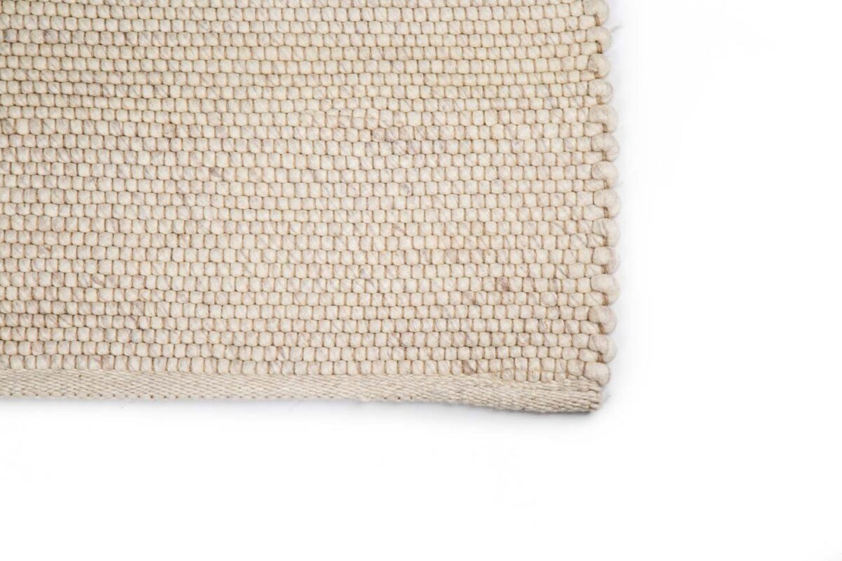 Close-up van de hoek van het Verona ST Cloud White 815 200x300 tapijt, met het eenvoudige geweven beige patroon tegen een witte achtergrond.