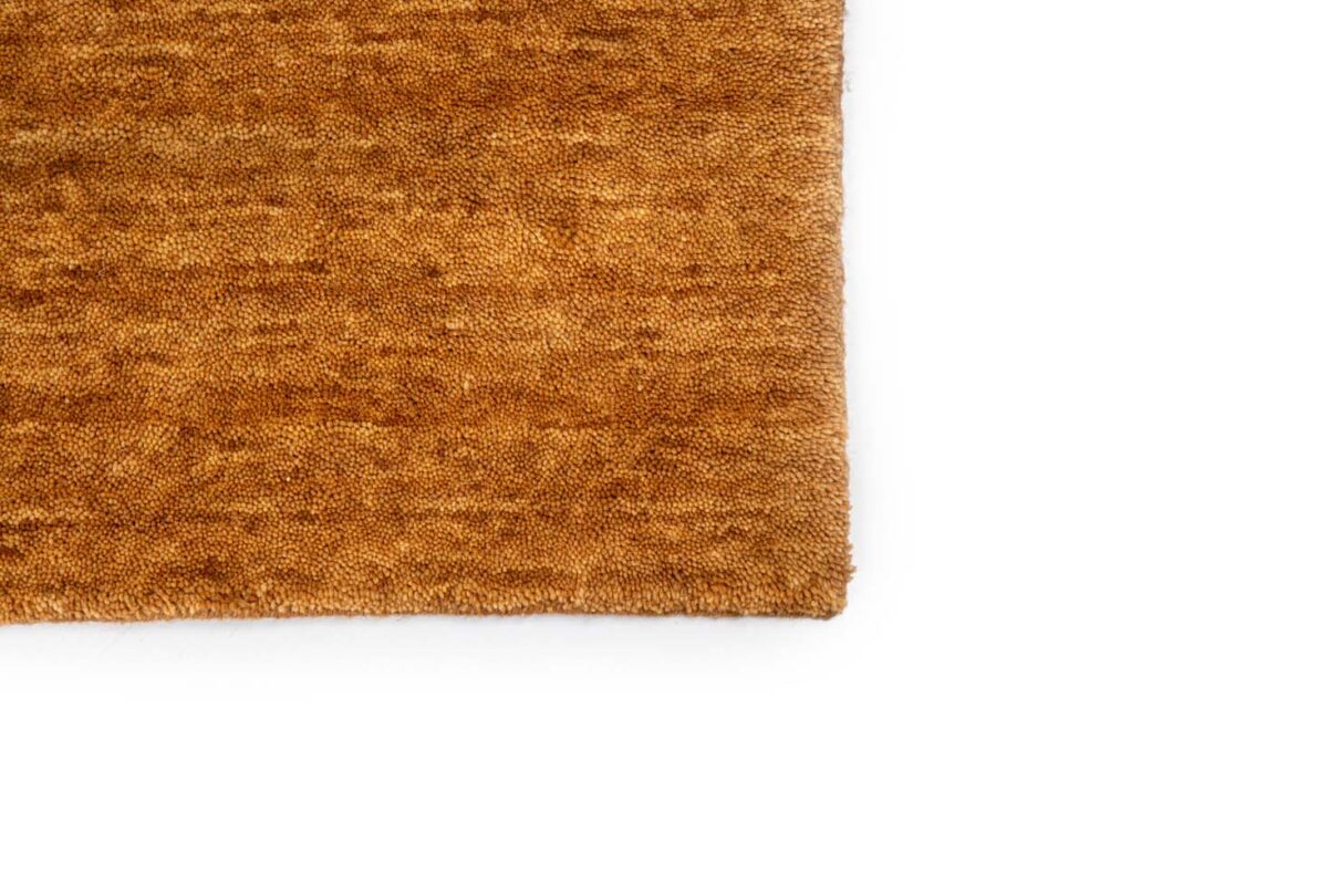 Close-up van de hoek van het San Stefano Rust 10 200x300 vloerkleed, met een bruin gestructureerd ontwerp op een wit oppervlak, waarbij slechts een deel van het vloerkleed zichtbaar is.