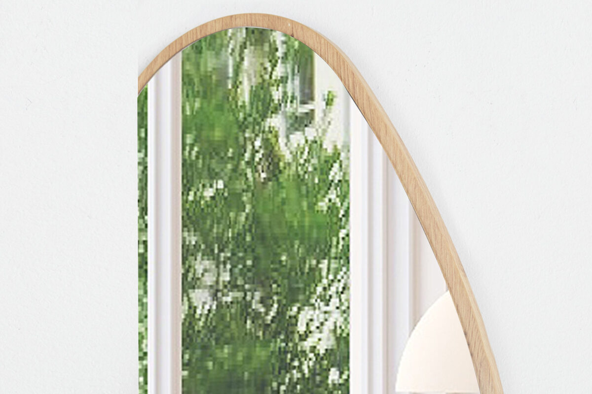 Een close-up van de Spiegel 'Rana' 80x50 Oude eik (1c), een gebogen spiegel met houten lijst die een groene boom met bladeren en een deel van een wit gordijn weerspiegelt, tegen een witte muur.