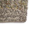 Close-up van de hoek van het Modena Beige 840 170x230 vloerkleed, met gestructureerd, geweven grijs en beige garen met subtiele gele en groene accenten, tegen een effen witte achtergrond.