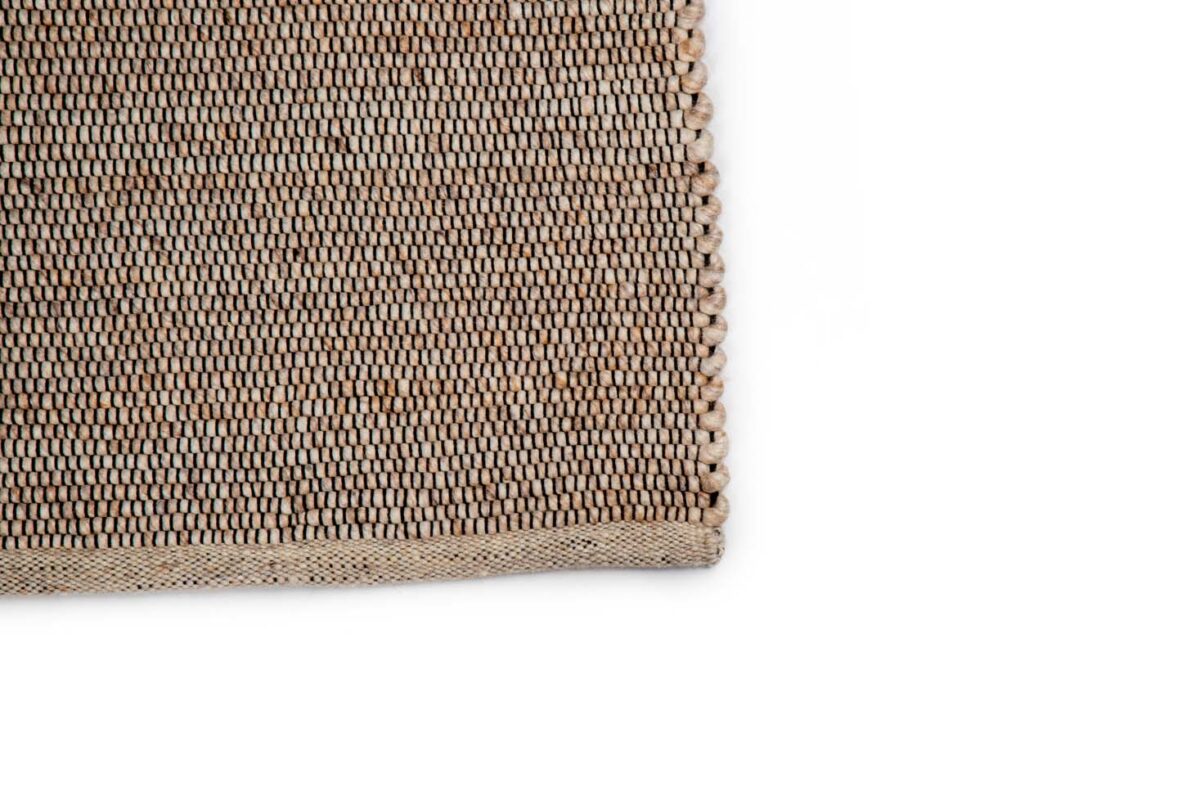 Close-up van de hoek van het Bressano Beige 142 170x230 tapijt, met gedetailleerde textuur en nette randen in natuurlijke beige en bruine vezels tegen een witte achtergrond.