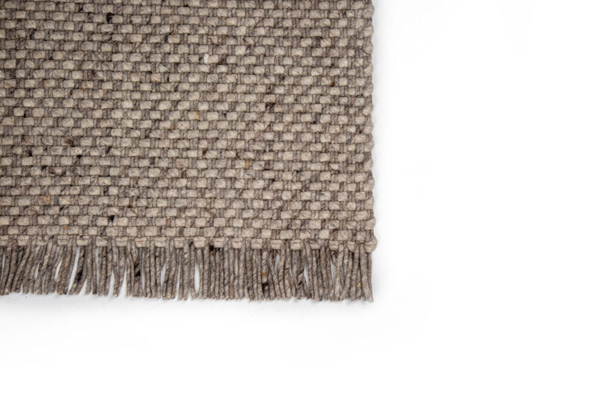 Een close-up van het Burano Dark Grey 618-613 200x300 tapijt toont de geweven textuur en franjes langs de onderrand op een witte achtergrond, waarbij alleen de linkerbenedenhoek van het rechthoekige tapijt zichtbaar is.