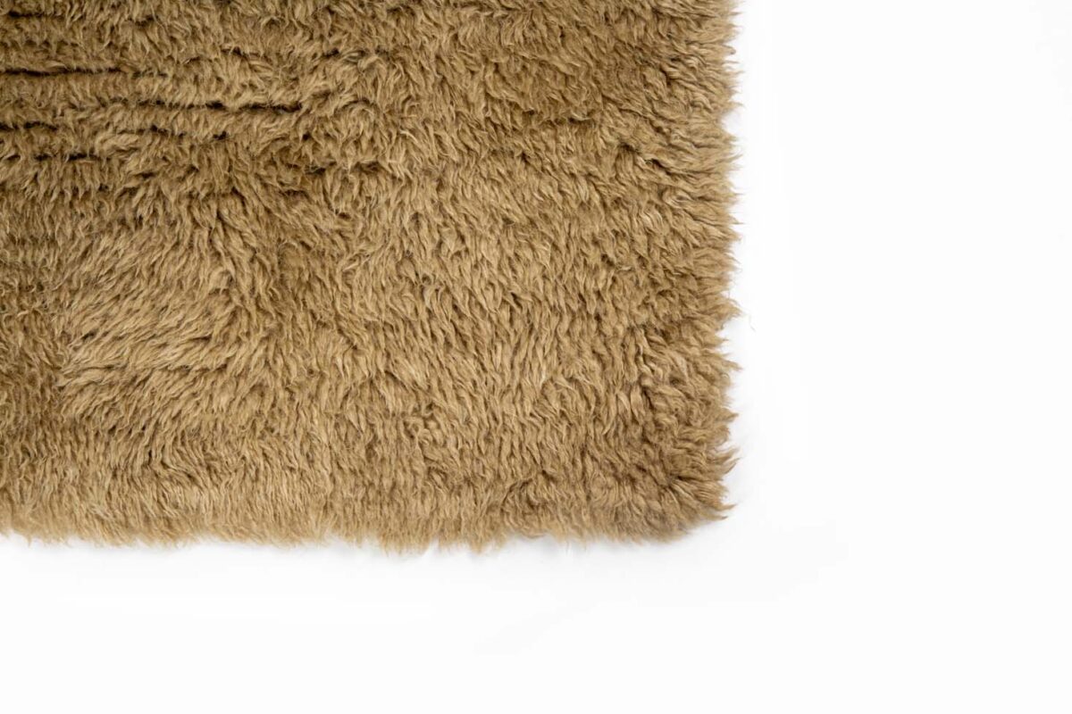 Close-up van de hoek van het Merano Beige 002 200x300 shaggy vloerkleed, getoond in bruine tinten op een witte achtergrond.