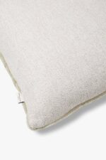 Een close-up van het Mohair sierkussenhoes Amy grijsgroen 50x50 cm, met een gestructureerde stof en een klein label op de naad, getoond tegen een witte achtergrond.