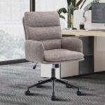 De Bureaustoel 'Aimé' Stof Fabb Raven 30 Zand staat bij een bureau met een monitor, toetsenbord, muis, plant en kantoorbenodigdheden in een lichte werkruimte met grote ramen.