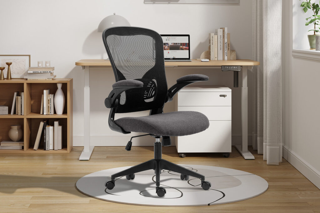 De Bureaustoel 'Marcos' Mesh Zwart/Grijs (1c), met een rugleuning van netstof en een gevoerde zitting op wieltjes, staat op een ronde mat bij een houten bureau met een laptop, lamp, boeken en decor in een licht, modern thuiskantoor.