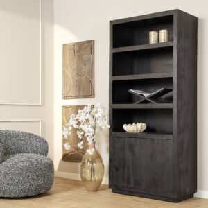 In een moderne woonkamer is de Boekenkast Brussel Zwart (90 cm) versierd met decor, een grote vaas met witte bloemen, abstracte muurkunst en een grijze fauteuil met structuur op een lichthouten vloer.