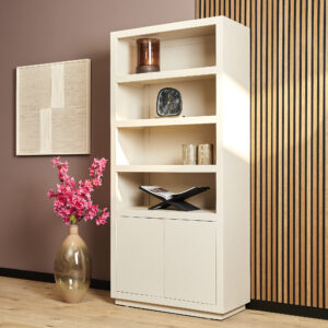 De Boekenkast Brussel 4 vakken, een moderne crèmekleurige boekenkast met decoratieve items op de planken, staat naast een grote vaas met roze bloemen, muurkunst met structuur en een accentmuur met houten panelen in een stijlvolle kamer.