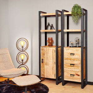 Een moderne woonkamer met een beige loungestoel en voetenbank, een ronde lamp met drie lampen en de Boekenkast Boaz | 1 deur-een houten boekenplank met zwart frame, gedecoreerd met decoratiespullen, een potplant en lades.