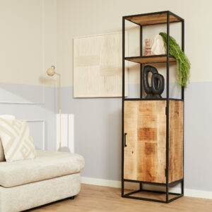 Een moderne woonkamer met een beige bank, de Boekenkast Denver mangohout en staal 1 deur holding decor en een hangende groene plant, een staande lamp en minimalistische muurkunst op lichte muren.