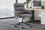 De Bureaustoel 'Aimé' Stof Fabb Raven 13 Donkergrijs ligt op een vloerbedekking naast een houten bureau met een computer, toetsenbord, plant en decor in een lichte kantoorruimte.