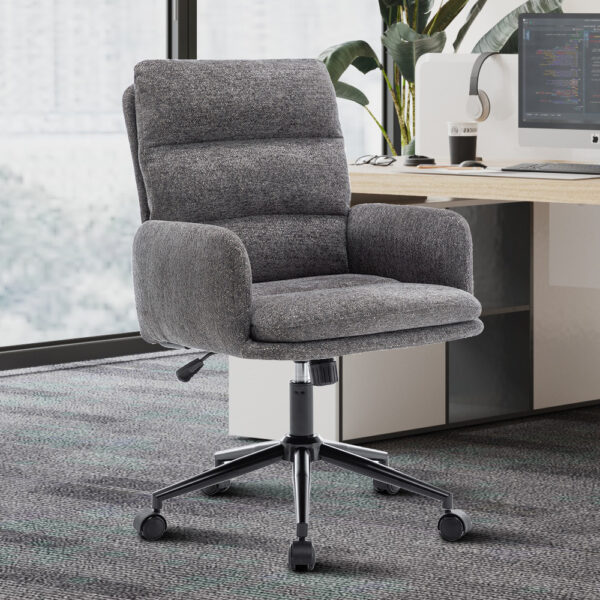 De Bureaustoel 'Aimé' Stof Fabb Raven 13 Donkergrijs ligt op een vloerbedekking naast een houten bureau met een computer, toetsenbord, plant en decor in een lichte kantoorruimte.