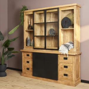 De Nashville Vitrinekast | 200 cm is een grote houten kast met lades, zwarte schuifdeuren en glazen bovenplanken om decor in uit te stallen. De kast wordt getoond naast een groene potplant in een moderne kamer met mauve muren en houten vloeren.