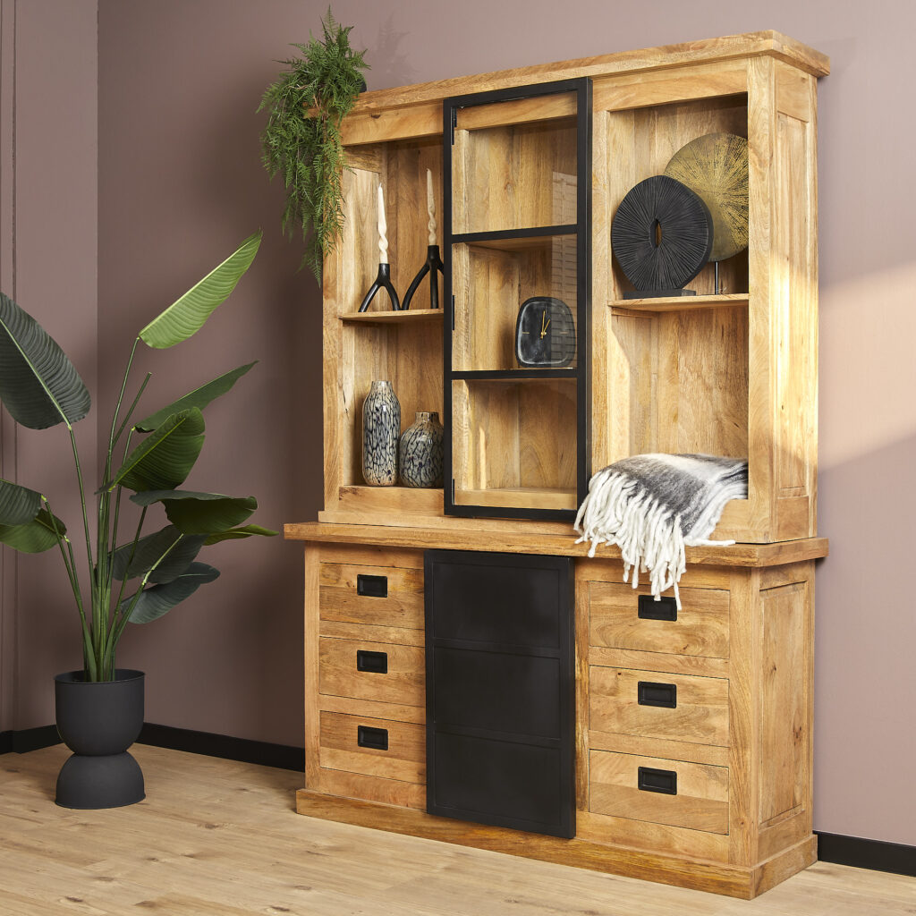 De Nashville Vitrinekast | 160 cm is een houten kast met planken, laden en een zwarte glazen schuifdeur. Hij is gestyled met vazen, beelden, een grijs kleed en een groene plant in potten bij een mauve muur.