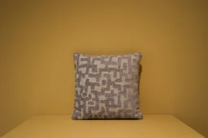 Het Armkussen 50x50, met een abstract grijs en beige geometrisch patroon met textuur, wordt getoond tegen een effen mosterdgele muur en oppervlak.
