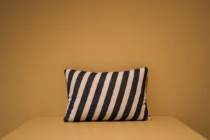 Een Armkussen 50x50 met zwarte en witte strepen rust tegen een effen mosterdgele muur op een bijpassend geel oppervlak.