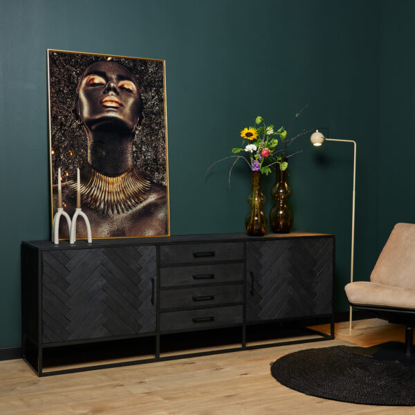 Een moderne woonkamer met donkergroene muren, het Dressoir New York | 210 cm zwarte dressoir, een portret met goudaccenten, vazen met bloemen, een witte staande lamp, een beige stoel en een rond zwart vloerkleed op een houten vloer.