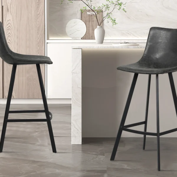 Twee Barstoel 'Ozan' PU Zwart krukken (set van 2) met slanke metalen poten staan in een keuken met lichte kasten, marmeren werkbladen en een minimalistische inrichting met een vaas van groene takken.