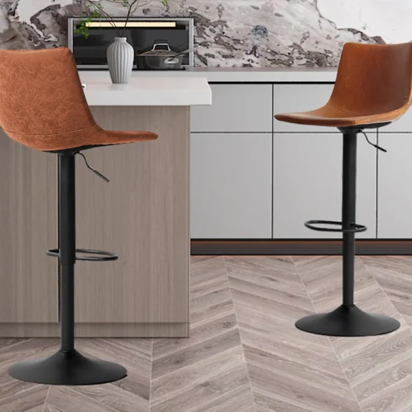 Twee 'Trevi' PU Cognac barkrukken (set van 2) met zwart metalen onderstel staan naast een lichthouten keukeneiland met witte werkbladen en kasten. De vloer heeft een visgraatmotief.