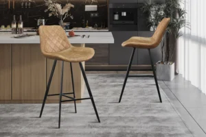 Twee 'Palmas' barkrukken in cognac PU met gewatteerde rugleuning en zwarte poten staan bij een keukeneiland met houten kastjes. De ruimte heeft donkere kasten, een ingebouwde espressomachine en een groot raam met transparante gordijnen.