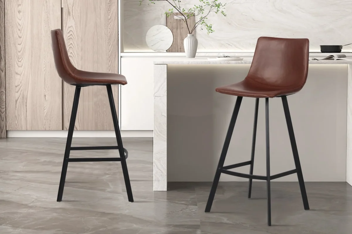 Twee Barstoel 'Ozan' PU Bruin barkrukken (set van 2) met zwart metalen poten staan in een strakke keuken met lichte kasten, marmeren aanrechtblad en een decoratieve vaas met takken op het aanrecht.