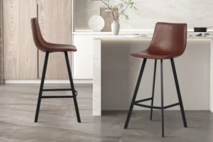 Twee Barstoel 'Ozan' PU Bruin barkrukken (set van 2) met zwart metalen poten staan in een strakke keuken met lichte kasten, marmeren aanrechtblad en een decoratieve vaas met takken op het aanrecht.