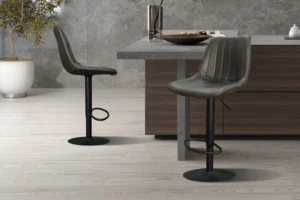Twee Barstoel 'Barcelona' PU Ote Topper 05 Donkerbruin barkrukken (set van 2) met donkere onderstellen en gestructureerde zittingen staan bij een houten keukeneiland in een minimalistische keuken met lichthouten vloeren, grijze stenen muren en een potplant op de achtergrond.