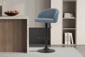 Een moderne keuken toont de SALE - Barstoel 'Arda' Bouclé Blauw (2 per doos) barkruk met zwart metalen onderstel naast een marmeren aanrecht, boeken en decor op planken, en een schaal met fruit zichtbaar op de achtergrond.
