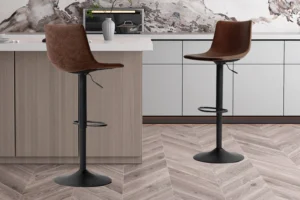 Twee Barstoel 'Trevi' PU Bruin barkrukken (set van 2) met zwart metalen onderstel staan in een moderne keuken met licht houten en witte kasten, een marmeren achterwand en een houten vloer met chevronpatroon.