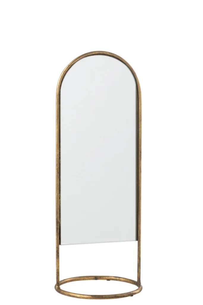 De Mirror On Foot Daisy Iron/Glass Gold heeft een hoog, gebogen ontwerp met een slank gouden frame en bijpassende ronde voet. De minimale maar elegante stijl geeft elke ruimte een moderne, decoratieve touch.