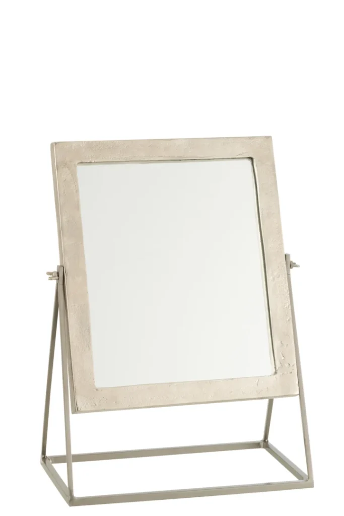 De Mirror Square On Foot Metal Silver heeft een vierkante metalen lijst met textuur, gemonteerd op een metalen standaard met een geometrische driehoekige basis om te kantelen. Afgebeeld tegen een effen witte achtergrond.