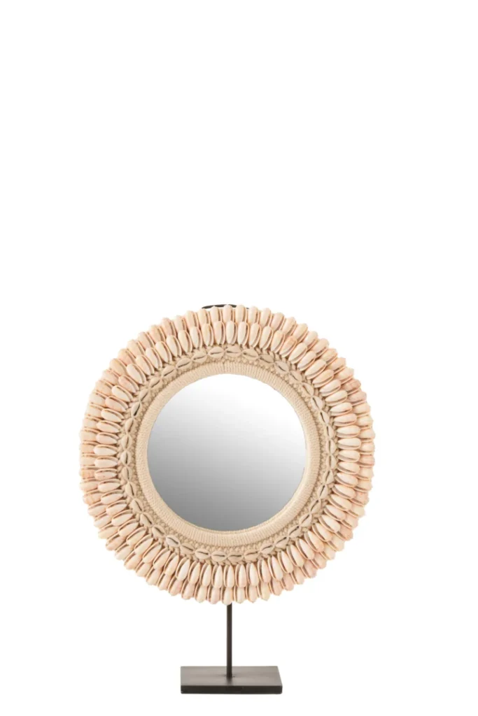De Mirror On Foot Mona Shells Light Pink Large heeft een ronde spiegel omlijst met lichtroze schelpen, gemonteerd op een slanke zwarte metalen standaard met een rechthoekige basis, en is geïsoleerd op een witte achtergrond.