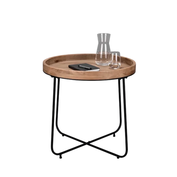 De Mirrors and More Bijzettafel JETTE, een ronde houten bijzettafel met zwarte metalen poten, toont een glazen karaf, een glas water en een gesloten notitieboekje met een pen op het oppervlak.
