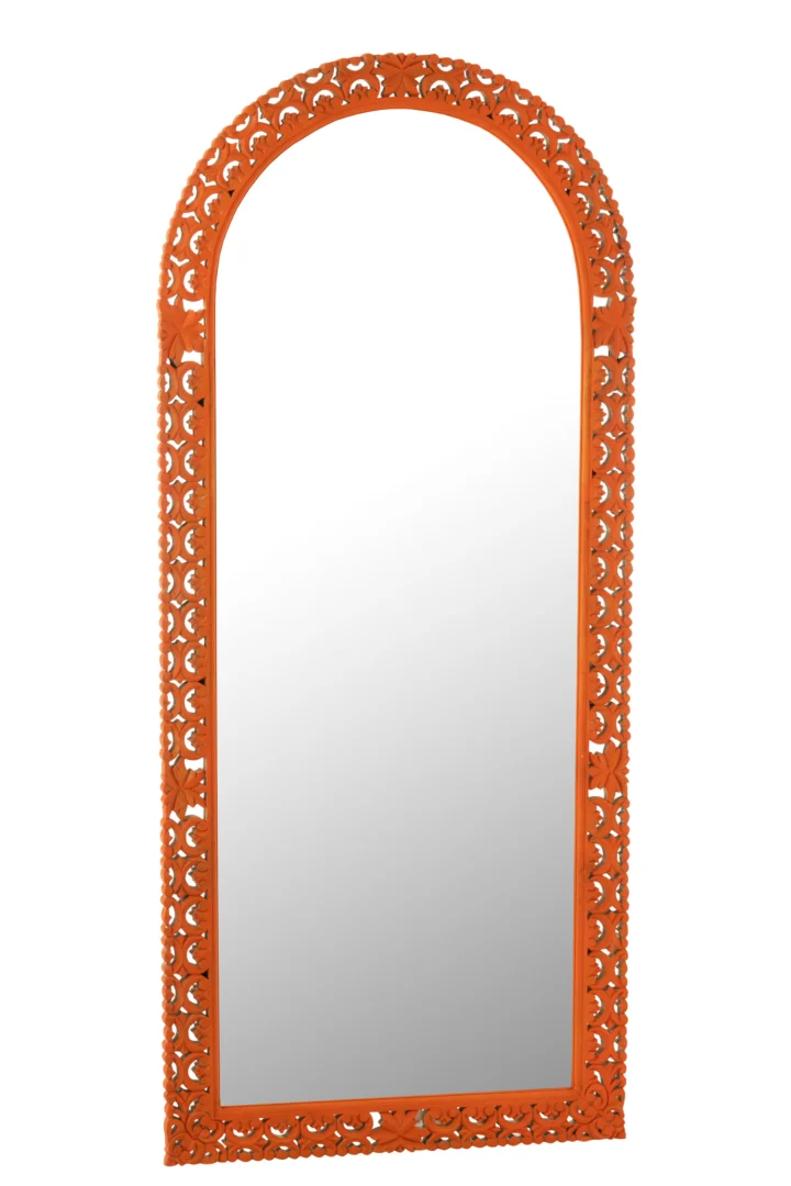 De Mirror Carved Mumbai Mango Wood Mix is een hoge, gewelfde spiegel met een sierlijke oranje lijst met ingewikkelde bloemmotieven rond de randen, rechtopstaand tegen een witte achtergrond.