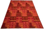 De Vloerkleed Afrikaans Polyacryl Mix Groot is een rechthoekig vloerkleed met een levendig geometrisch patroon in rode, oranje en roze tinten met herhalende ruitvormige en rechthoekige vormen.