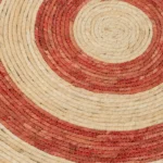 Een close-up van de Vloerkleed Rond Cirkels Maïsschil Oranje/Rood Medium (Set van 2) toont de geweven concentrische cirkels in natuurlijke beige en oranjerode tinten, die de gedetailleerde verweven vezelstructuur benadrukken.