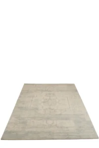 De Vloerkleed Jacquard Wol Beige/Blauw is een vierkant vloerkleed met lichtbeige en grijze tinten met een vervaagd, verweerd patroon op een effen witte ondergrond.