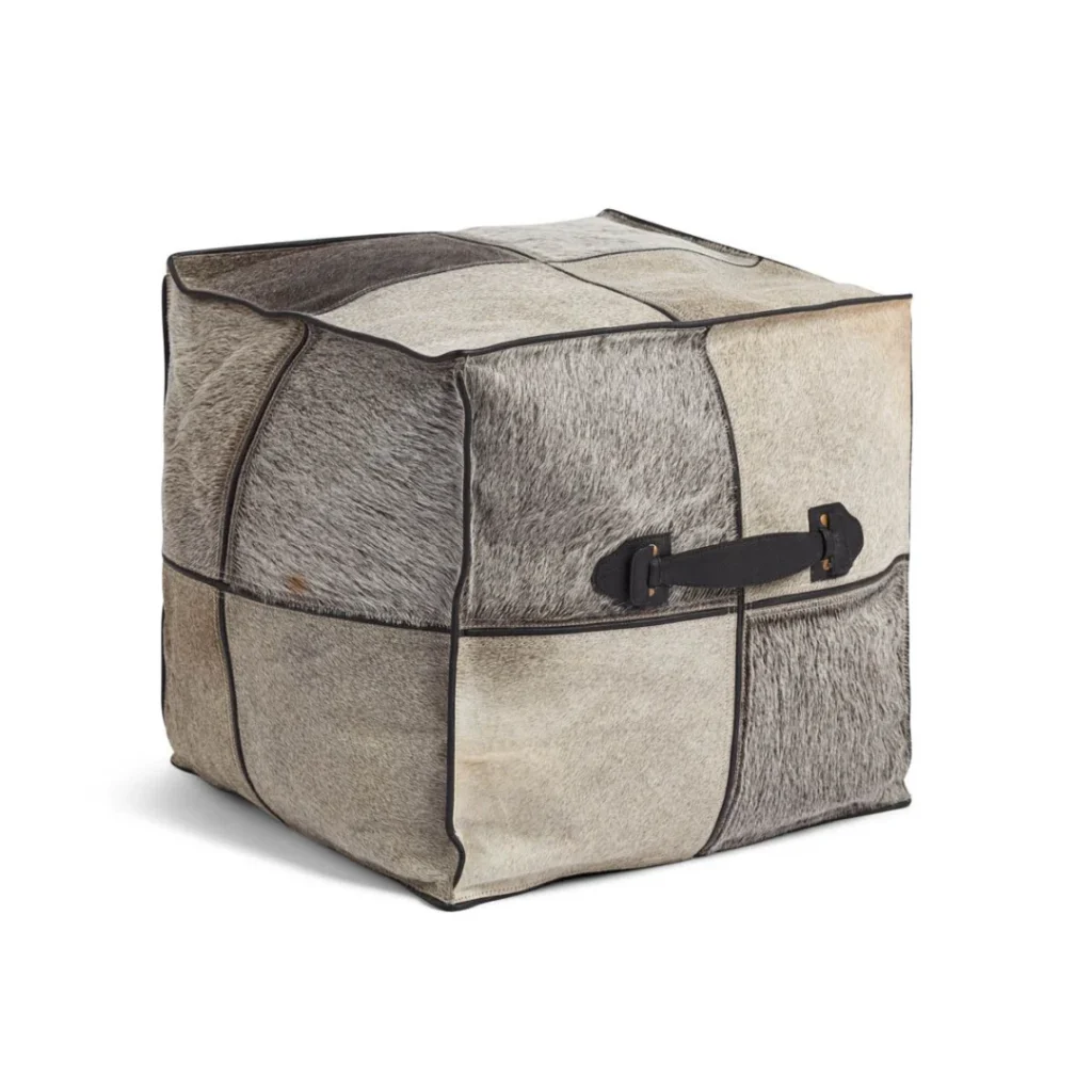 De Kalfslederen Poef Vierkant Handvat V02 is een vierkante voetenbank met grijs en beige koeienhuid patchwork, zichtbare stiksels en een zwart leren handvat aan één kant.
