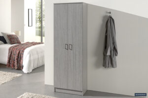 Een moderne slaapkamer met de Opbergkast 'Ray' met 2 deuren en 4 planken in grijs eiken, een badjas aan een wandhaak en een opgeruimd bed met een wit dekbed en geruite deken. Zonlicht stroomt door een raam op de achtergrond.