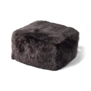 De Poef Schapenvacht Lange Wol L01 is een vierkante voetenbank met donkere, pluizige bekleding van imitatiebont op een effen witte ondergrond.