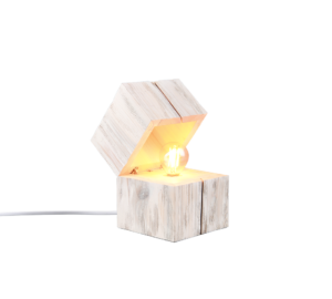 De TRIO Tafellamp TREASURE is een kubusvormige, witgekalkte houten lamp met een schuine open bovenkant die een gloeiende lamp binnenin onthult. De lamp staat op een plat oppervlak met een netsnoer dat uit de achterkant steekt.